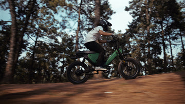 Action shot of the Pawkymo AR50 2X2 electric bike in green, riding on rugged terrain in a forest, showcasing its off-road capability and smooth performance.